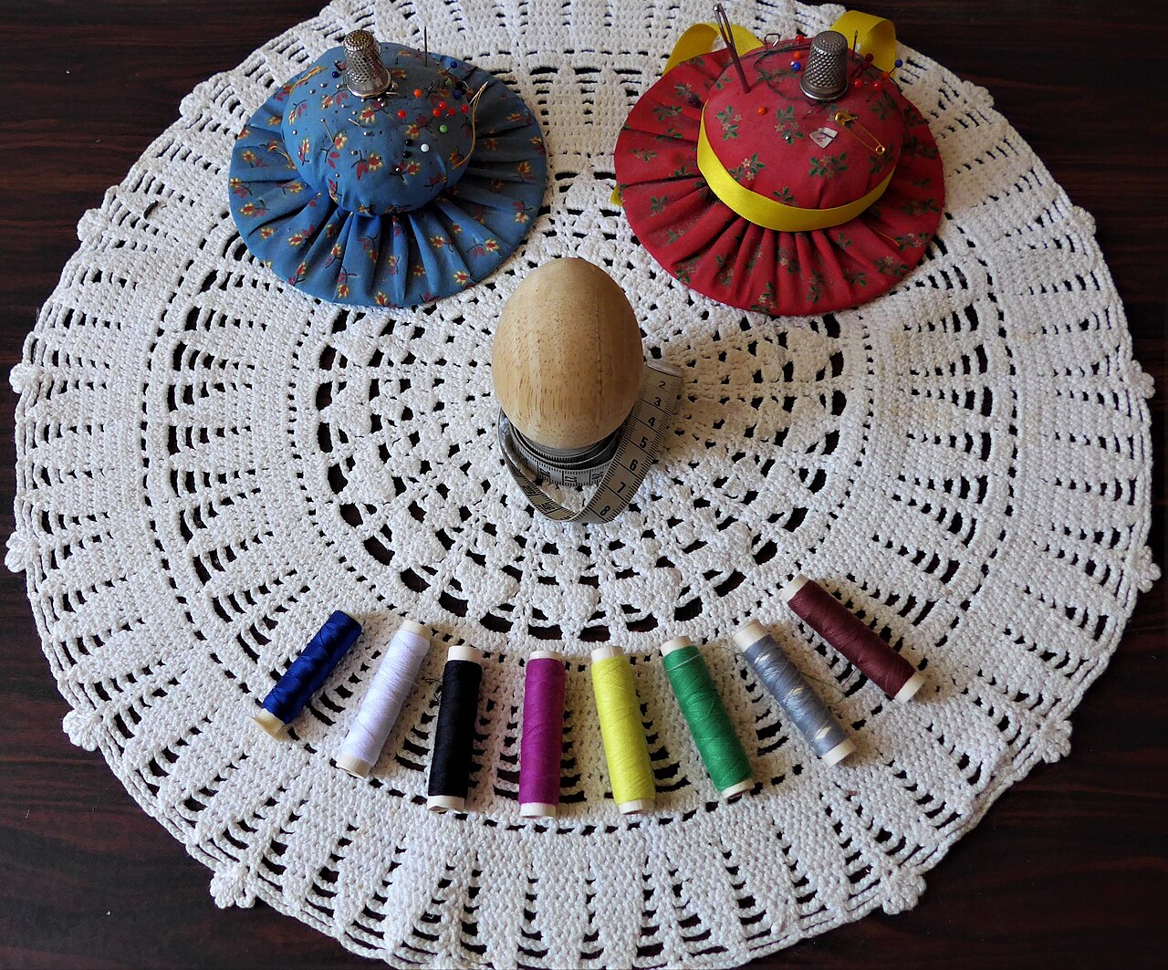 Sewing kit with thread spools and pincushions on a lace doily